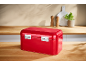 Glossy red bread bin on a wooden countertop with kitchen accessories in the background.