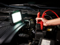 Work light illuminating a car engine while jump-starting with booster cables.