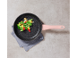 Frying pan with a pink handle, filled with stir-fried vegetables on a grey cloth.