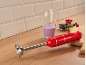 Red immersion blender on a wooden countertop with smoothie and berries.