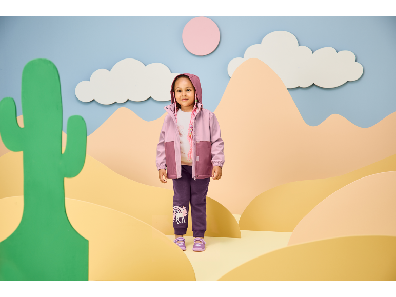 Smiling girl in a pink and purple hooded jacket and purple sweatpants with a unicorn print.