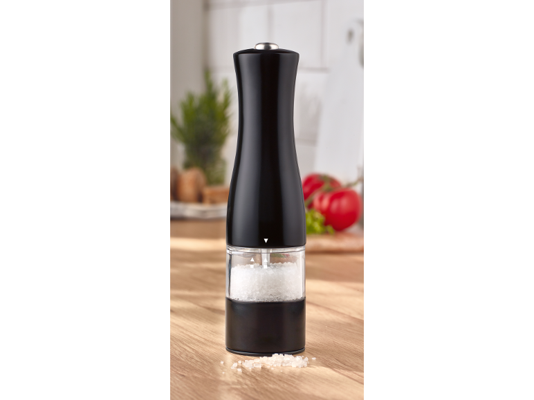 Black salt grinder with coarse salt on a wooden kitchen counter.