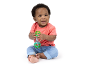 Smiling baby in a coral t-shirt and jeans, playing with a green rattle.