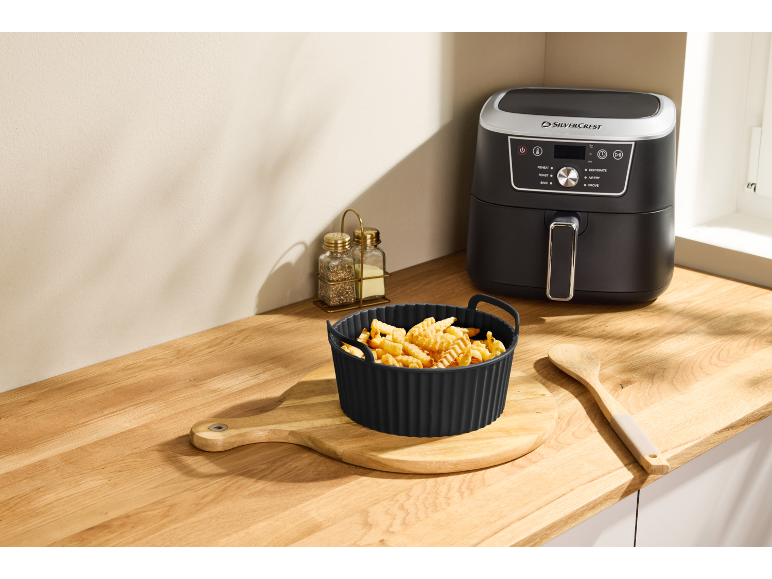Air fryer with a bowl of crinkle-cut fries on a wooden kitchen counter.