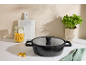 Black pot with lid, jar of pasta, cutting board, and basil plant on a countertop.