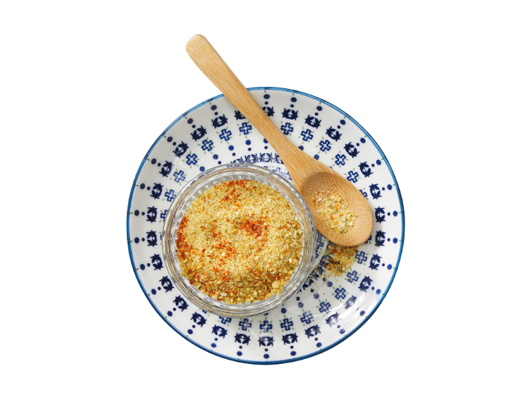 Overhead view of a glass bowl of spice mix and a wooden spoon on a white and blue plate.