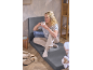 Woman drinks coffee, sitting on a grey floor chair, with beige clogs on the floor.