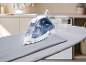 Steam iron on an ironing board with a measuring cup in a laundry room.