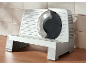 Gray meat slicer with a metal blade on a wooden surface next to a tiled wall.