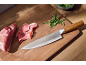 Chef's knife with wooden handle, raw meat, and arugula on a wooden cutting board.