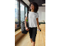 Woman in white t-shirt and black capri leggings, with a bag and water bottle.