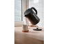 Black kettle pouring hot water into a mug on a wooden countertop.
