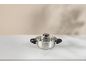Stainless steel pot with a glass lid on a white marble surface.