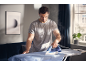 Man ironing a blue shirt on an ironing board with a steam iron.