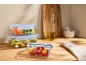 Glass food storage containers with vegetables and pasta on a wooden countertop.