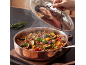 Man contentedly smelling steaming ratatouille in a copper pot.