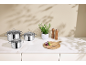Stainless steel pot set with glass lids, fresh herbs, and a cutting board with vegetables.