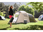 Woman with sleeping bag and cooler next to a tent at a campsite.