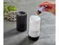 Hand adding lavender oil to a black diffuser with lavender on a grey background.
