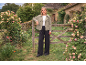 Woman in a khaki jacket and black wide-leg trousers leaning on a wooden fence with roses.