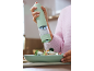 Hand holding an electric salt grinder, seasoning a fresh salad on a light green plate.