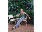 Woman in blue patterned trousers and wedge sandals in a flowery courtyard.