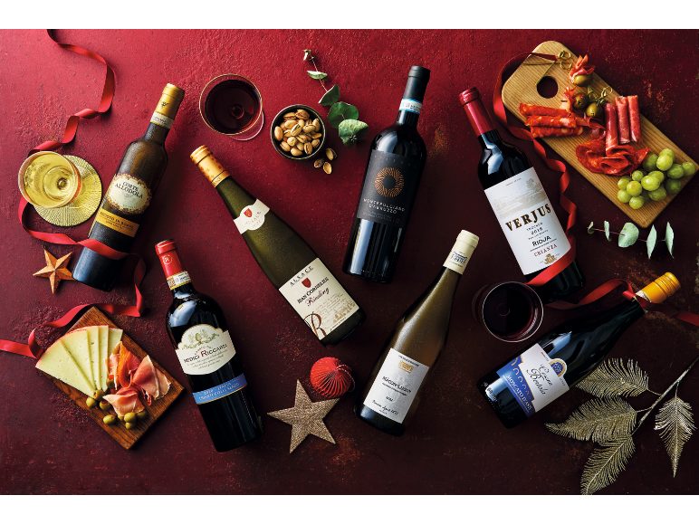 Several bottles of red and white wine with glasses, appetizers, and festive decorations on a red background.