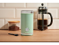 Coffee grinder, ground coffee jar, and French press on a kitchen counter.