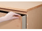 Hand opening a light wooden drawer in a wooden cabinet.