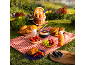 Picnic blanket filled with croissants, fruits, and sunscreens on green grass.