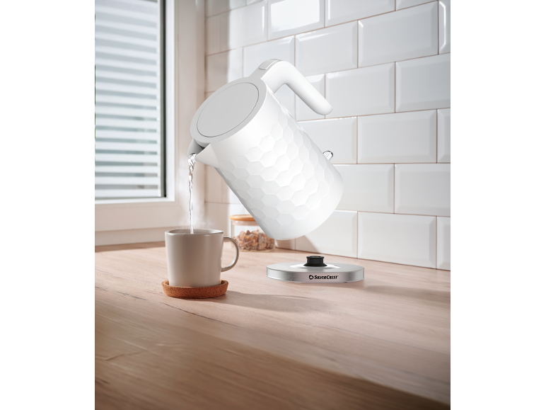 White electric kettle pouring hot water into a mug on a wooden kitchen counter.