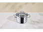 Stainless steel pot with a glass lid on a white countertop.