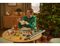 Man in Christmas sweater wrapping gifts, with wrapping paper and ribbons on table.