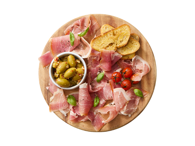 Wooden board with serrano ham, olives, cherry tomatoes, and toasted bread.