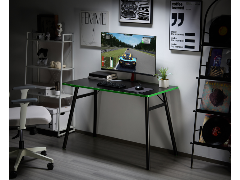 Black gaming desk with green accents, monitor, office chair, and shelving units.