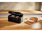 Black bread bin with bread and sliced wholemeal bread on a wooden countertop.