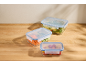 Three glass food storage containers with various vegetables and fruits on a wooden table.