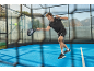 Man in sportswear playing padel on a blue court.