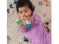 Baby in a purple romper playing with a colorful rattle on a textured rug.
