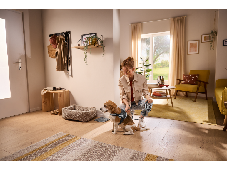 Woman prepares dog for walk, holding leash, in cozy hallway with wooden furniture.
