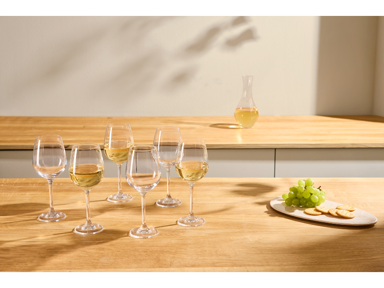 White wine glasses, a wine carafe, grapes, and crackers on a table.