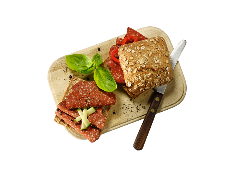 Whole grain bread sandwiches with salami, bell pepper, basil, and cucumber on a wooden board.