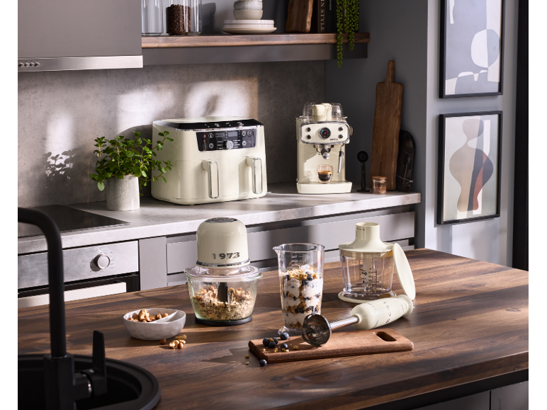 Kitchen with cream air fryer, espresso machine, and food processor, preparing breakfast.