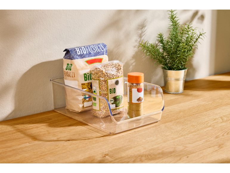 Clear organizer with organic pasta, lentils, and spices on a wooden countertop.