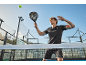 Man in black sports outfit playing padel with a racket and a ball on a court.