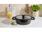 Black pot with a glass lid on a countertop, surrounded by pasta, basil, and kitchen utensils.