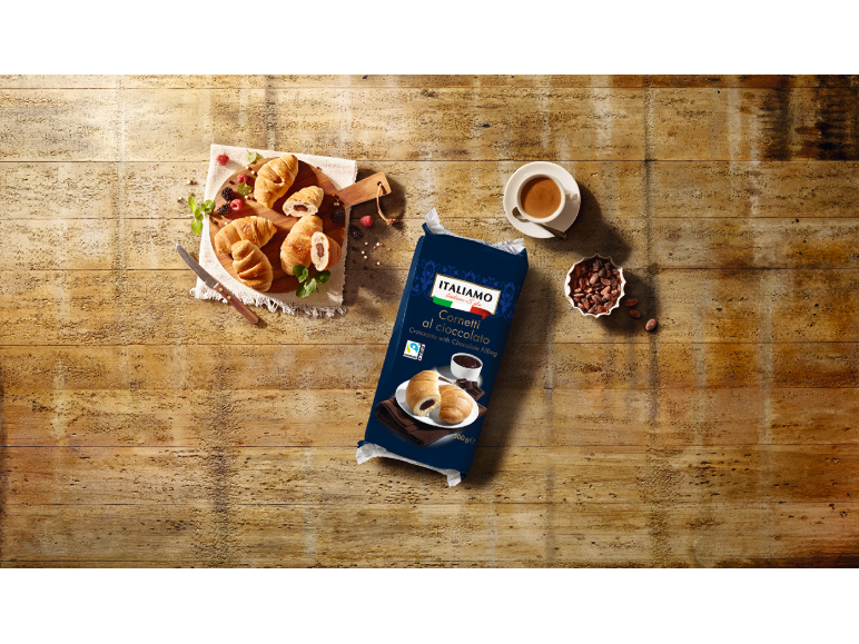 Chocolate croissants on a wooden board with berries, coffee, and a pack of croissants.