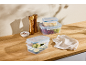 Plastic food containers, wooden salt and pepper grinders, and a kitchen towel on a wooden table.