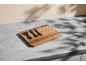 Wooden cheese board with black cheese knives on a grey table.