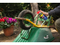 Man lubricating a wheelbarrow wheel with a spray, with flowers in the background.